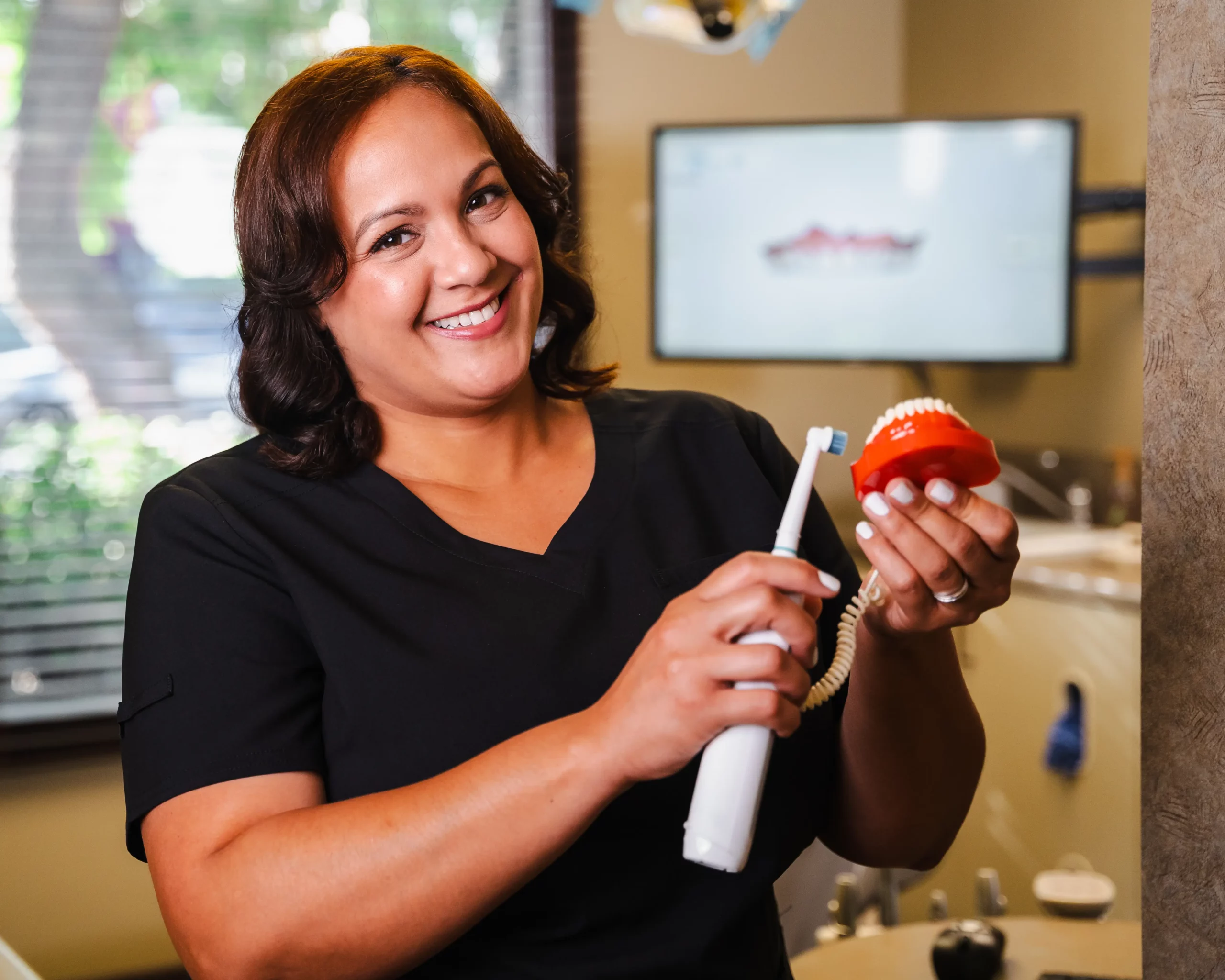 Team member smiling while holding an electric toothbrush and a model of teeth